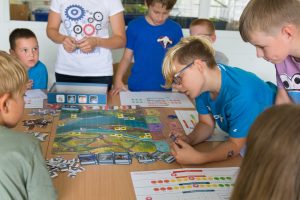 Dzieci w szkole grają w grę planszową Mosty, pochylają się nad stołem z kolorowąplanszą