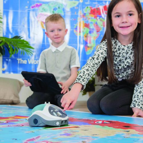 dziewczynka i chłopiec programują ruchy robota Loti-Bota na macie z mapą świata