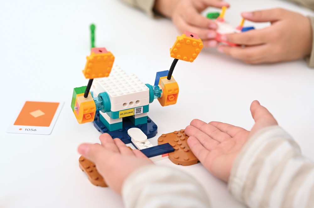 program cyfrowy uczeń dziecko wyciąga dłonie do modelu zbudowanego z klocków lego education